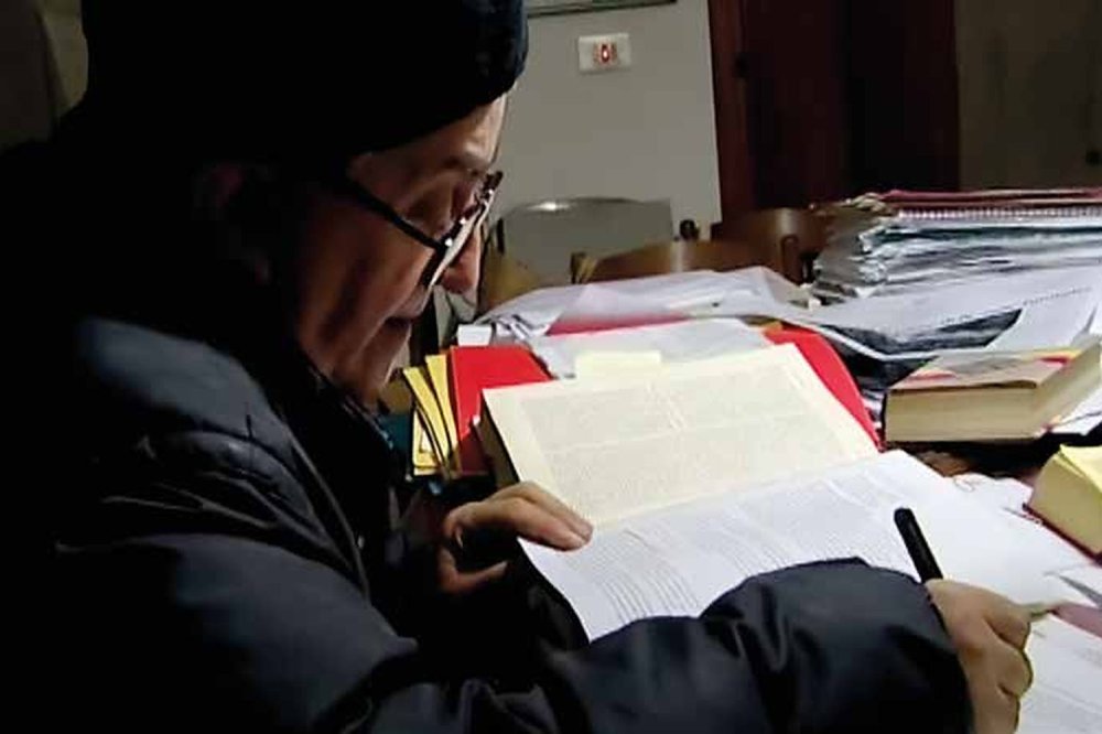 Don Oreste Benzi scrive i commenti per Pane Quotidiano, immagine storica Don Oreste Benzi alla scrivania, circondato da libri, mentre scrive i commenti alla Parola per Pane Quotidiano
