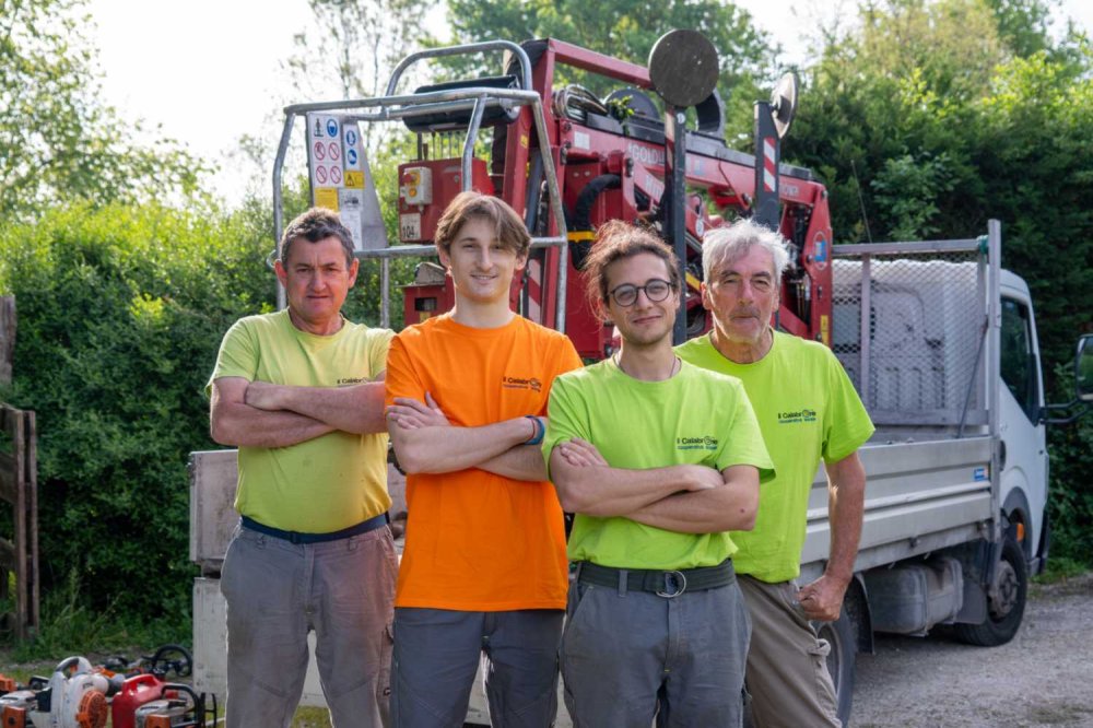 Quattro operatori della squadra aree verdi della cooperativa Il Calabrone davanti ai mezzi di lavoro