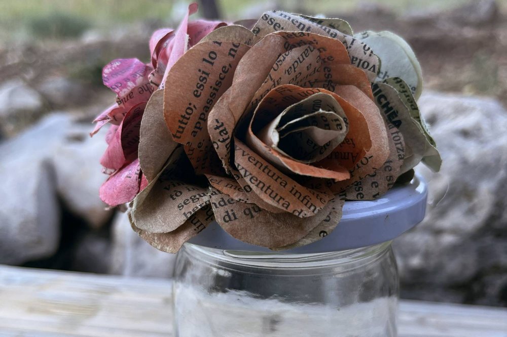 Una rosa realizzata con le pagine di Pane Quotidiano posata su un barattolo di vetro