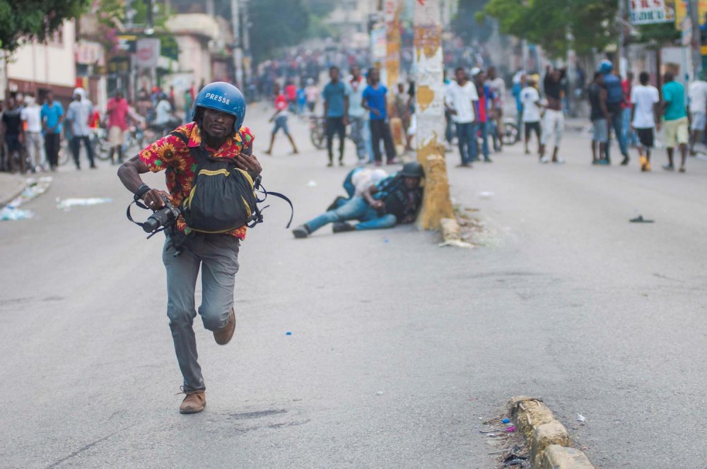 Un giornalista corre tra la gente che protesta contro il presidente Moise.