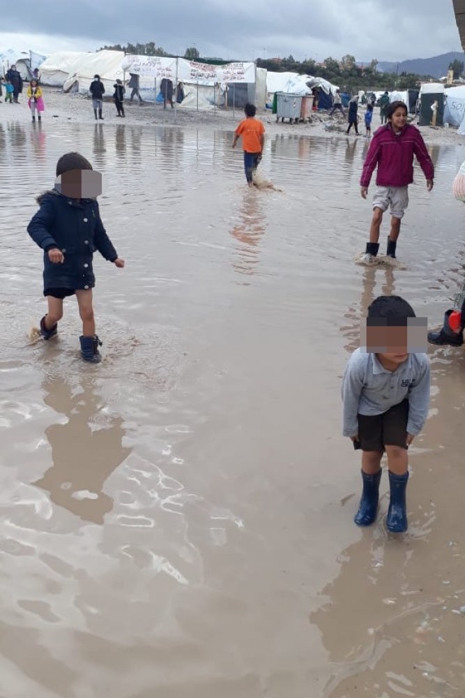 Bambini giocano nell'acqua che allaga il campo profughi