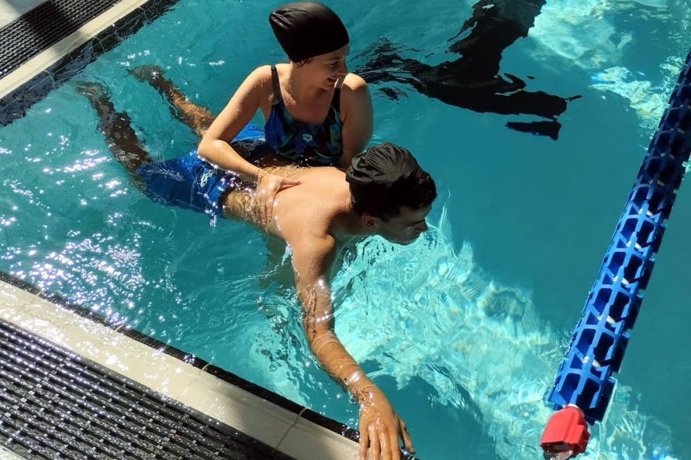 Ragazzo in piscina aiutato da istruttrice