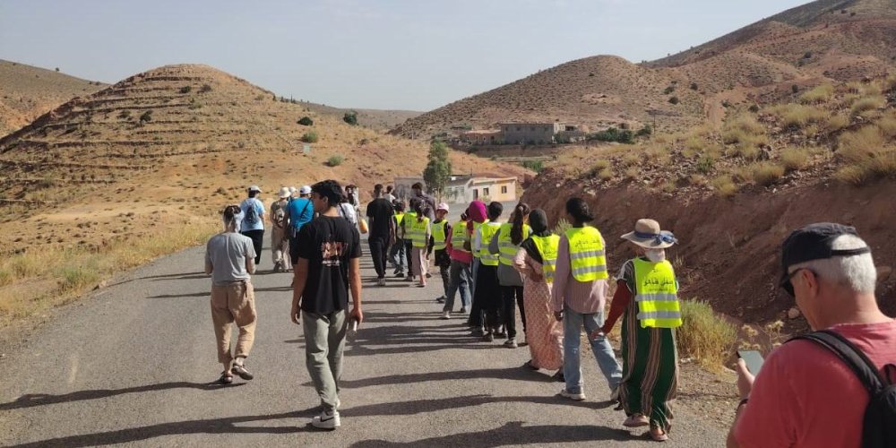 Gruppo di volontari e bambini con il gilet giallo cammina su una strada tra le colline dellAtlante