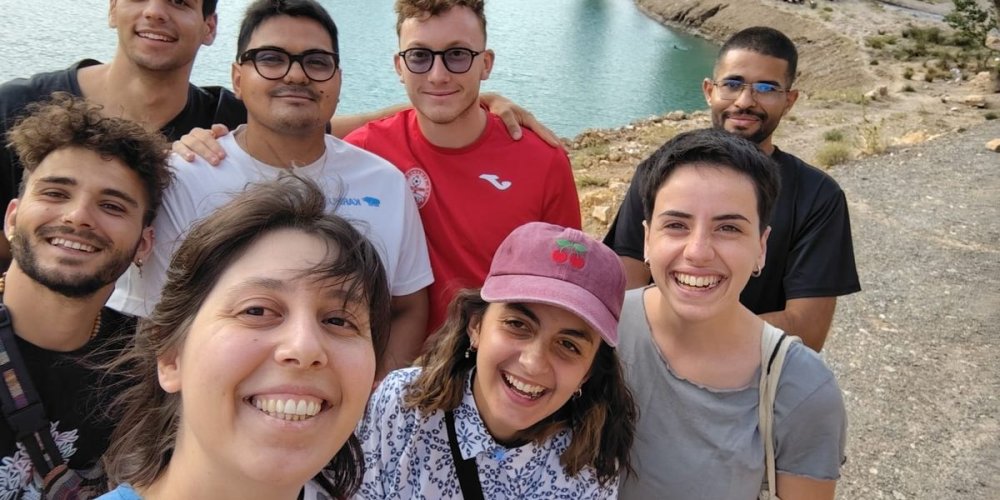Selfie di gruppo degli otto giovani con un lago sullo sfondo