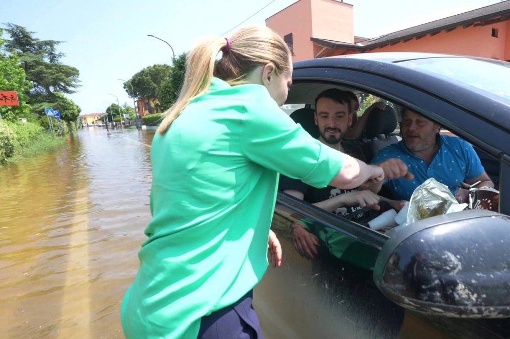 Giorgia Meloni di spalle con alluvionati in auto, su una strada allagata