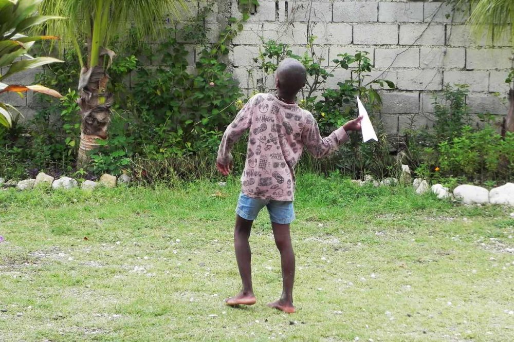 Un bambino lancia un aereoplano di carta oltre il muro della missione