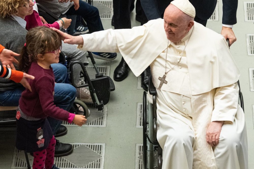 Papa Francesco in carrozzella a rotelle accarezza una bambina